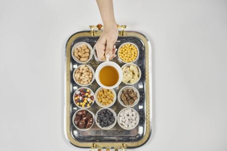 Ramadan Kareem background. Female hands holding a cup of tea over Ramadan food and sweets. Little cups filled with iftar sweets and snacksの写真素材