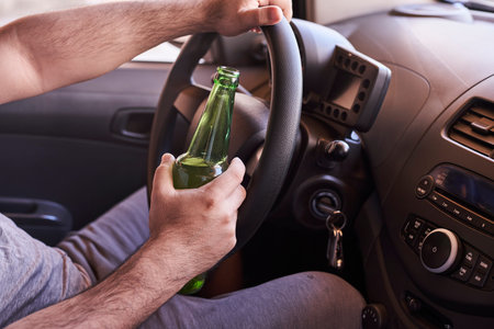 An unrecognizable man drinking beer while driving car. Concepts of driving under the influence,...