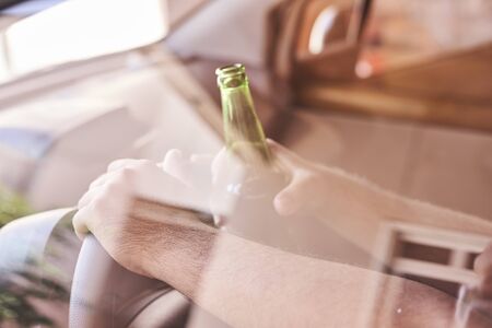 An unrecognizable man drinking beer while driving car. Concepts of driving under the influence, drunk driving or impaired drivingの写真素材