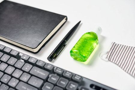 Work from home. Beautiful arrangement of keyboard, face mask, antiseptic gel and black notepad....