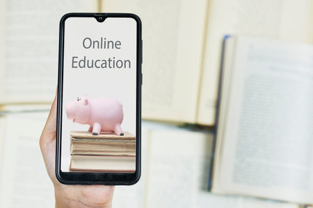 Cost of online education. Person hold smartphone with image of piggy bank and books. Copy space