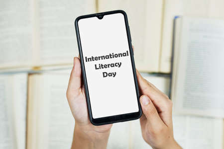 September 8 - International Literacy Day. Woman holding smartphone over books backgroundの写真素材