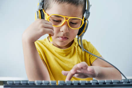 An adorable kid in a yellow t-shirt with a headphone listening online course. Boy typing on pc keyboard. Homeschooling. Cute mixed-race schoolboy learning a foreign language onlineの写真素材