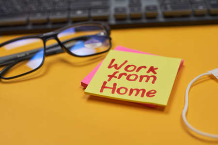Computer keyboard, eyeglasses, face mask and sticky notes on the yellow background with Work from home textの写真素材