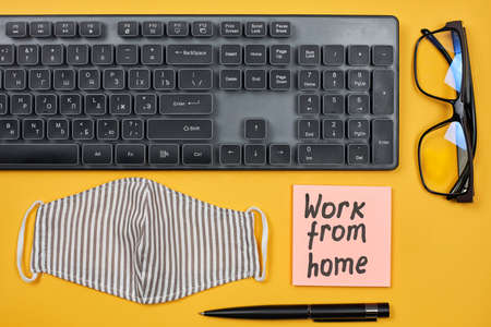 Computer keyboard, eyeglasses, face mask and sticky notes on the yellow background with Work from home textの写真素材