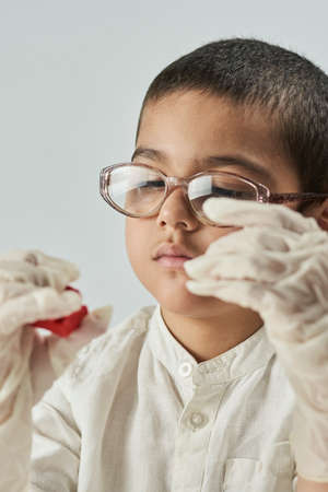 Close-up portrait of mixed raced child in glasses and gloves experimenting with slimeの写真素材