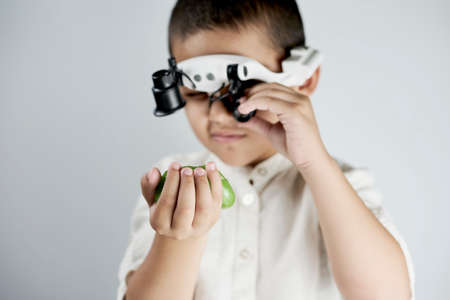Little boy holding a slime and looking on it through the special magnifying eyeglasses headsetの写真素材