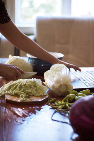 Young woman preparing healthy salad. Housewife watching popular food blogger on laptop, and making vegetrarian salad. Healthy vegetable food recipeの写真素材