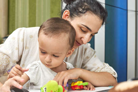 Mommy talking on the phone. Working from home due to coronavirus. A young middle-eastern woman trying to work at home while sitting with her baby boyの写真素材