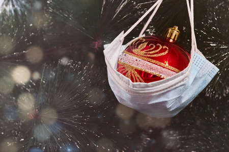 Celebrating winter and Christmas holidays in the new Covid-19 reality. Christmas toy hanging on the Xmas tree with a medical face mask. Merry healthy Christmasの写真素材