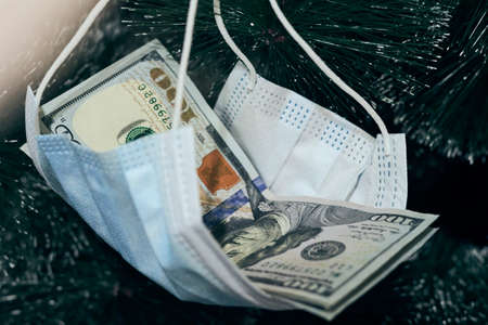 US dollars hanged with face mask on the Christmas tree as a gift. Celebrating winter and Christmas holidays in the new normal with coronavirus infectionの写真素材