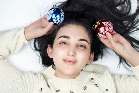 Overhead view of a cute mixed-race woman lying down and holding in hands Christmas ornamentsの写真素材