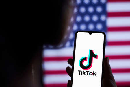 Tashkent, Uzbekistan - 16 September 2020: Woman using the TikTok app. TikTok block, ban in the US. Female holds a smartphone with the TikTok logo against the American flagのeditorial素材