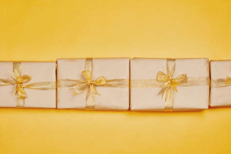 Row of Christmas present boxes on yellow background. Christmas gifts wrapped on craft paper and tied with golden ribbonの写真素材