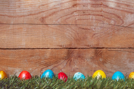 Colorful Easter eggs on the grass. Decorated easter eggs on placed on green grass against the wooden desk with copy spaceの写真素材