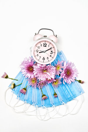 Spring lockdown. Fresh spring flowers and alarm clock on face masks. Concept of quarantine in spring dueの写真素材