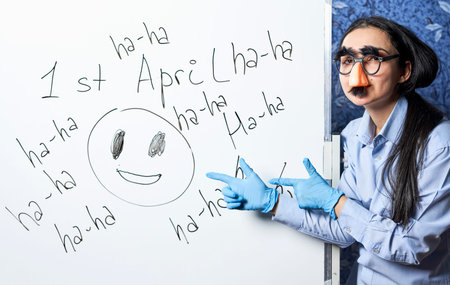 April fools day jokes. A woman in a funny foolish mask having fun near the chalkboard. Celebrating...