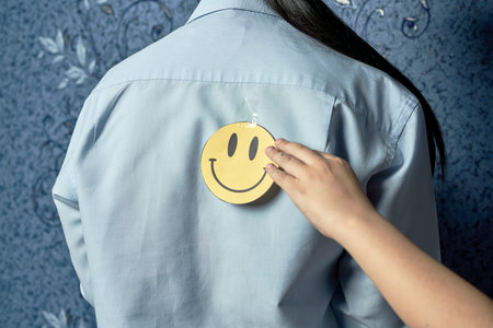 April fools day jokes. Son putting funny smile face sticker onto moms back. A funny sticker on...