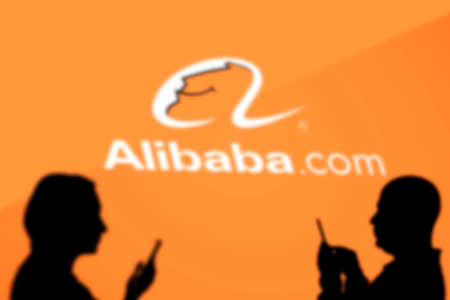Tashkent, Uzbekistan - March 4, 2021: Silhouette of people over Alibaba.com logotype - popular Chinese platform for global wholesale trade, who serve millions of buyers and suppliers around the worldのeditorial素材