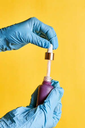 Female hand holding nail polish bottle over colored background. Hand in blue medical gloves holding a nail polish stick with gelの写真素材