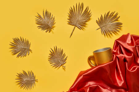 Decorative golden leaves on red textile backdrop. Bright, glamour autumnal concept with fake fall leaves on red silk backdropの写真素材