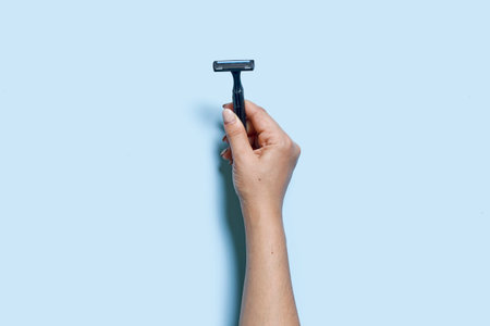 A person hand holds a multiple use shaving razor on blue background. View from aboveの写真素材