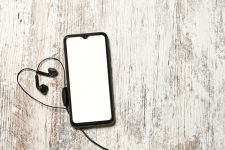Mobile phone with empty screen and earphones on bright wooden backgroundの写真素材