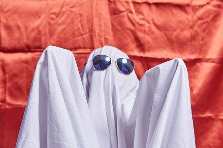 White ghost on orange. Halloween holiday. A young child dressed in a ghost costume for Halloween on...