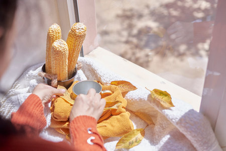 Corns, autumn leaves, pine cones and coffee cup on windowsill. Creative autumnal background near the windows in a sunny autumn dayの写真素材