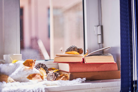 Bright autumn background with books and coffee mug. Reading a book in a sunny autumnal day on the windowsill. Spending cold weekends in cozy homeの写真素材