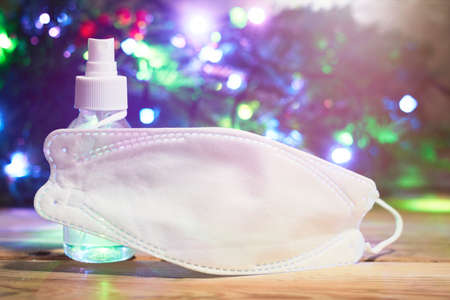 Christmas holidays. Medical face mask and antiseptic gel over decorated with lights Christmas tree backgroundの写真素材
