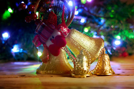 Golden Christmas bells on wood. Merry Christmas concept. Xmas decorations over decorated festive Christmas treeの写真素材