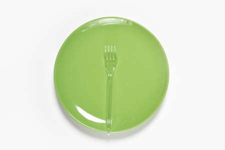 Green plate and plastic fork with spoon on green background. Copy spaceの写真素材