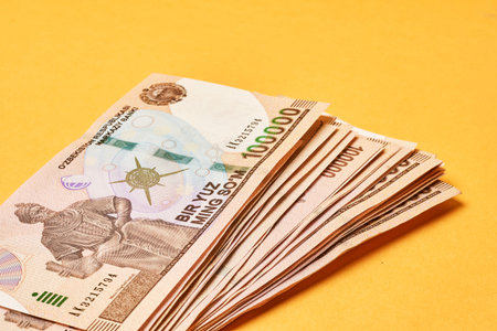 Pile of Uzbek sums on yellow. Uzbek currency money bill. A stack of one hundred thousand Uzbek sum....