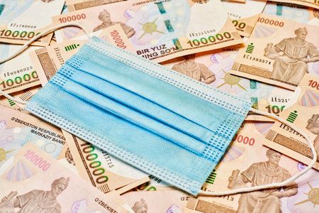 Uzbek currency sum weakening during pandemic. Pile of Uzbek sum currency money bill and medical face...
