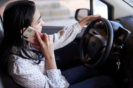 Unsafe driving. Young multiracial woman talking on the phone while driving. Distracted Driving. Female driving and talking on cellphoneの写真素材