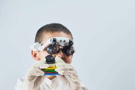 A boy in head magnifying glasses headset learning Incredible chemistry of plastiline. Tactile play or sensory play for older kidsの写真素材