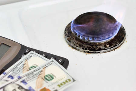 Burning gas stove burner, calculator and US dollar banknotes. Pay for natural gas, bill, tariff. Pile of coins and burning fire gas stove hob and money. Calculating gas tariff or costの写真素材