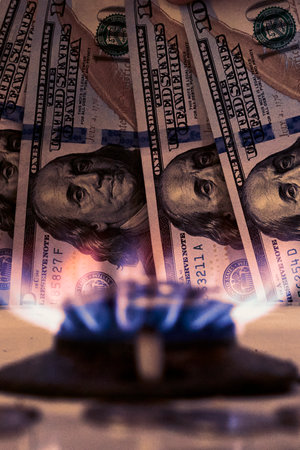 Burning gas stove burner and US dollar banknotes. Pay for natural gas, gas bill, tariff. Pile of coins and burning fire gas stove hob and moneyの写真素材