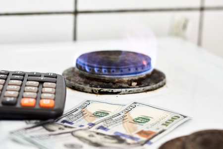 Burning gas stove burner, calculator and US dollar banknotes. Pay for natural gas, bill, tariff. Pile of coins and burning fire gas stove hob and money. Calculating gas tariff or costの写真素材