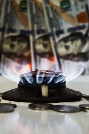Burning gas stove burner and US dollar banknotes. Pay for natural gas, gas bill, tariff. Pile of coins and burning fire gas stove hob and moneyの写真素材