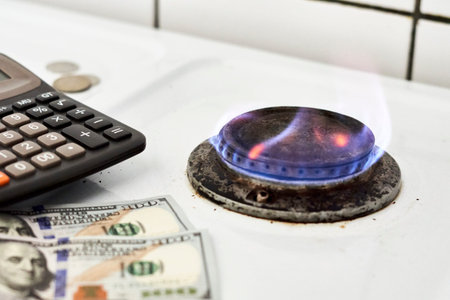 Burning gas stove burner, calculator and US dollar banknotes. Pay for natural gas, bill, tariff. Pile of coins and burning fire gas stove hob and money. Calculating gas tariff or costの写真素材