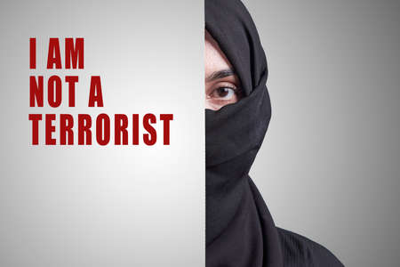 Young Muslim women with covering part of face and saying - I am not a terrorist. Muslim girl in traditional nikab clothing. Symbol of discrimination, stereotypes, racism and Islamophobiaの写真素材