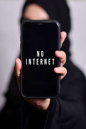 Muslim woman holding smartphone with text - No internet. Symbol internet restrictions, censorship or blocked access to global network in Islamic countryの写真素材