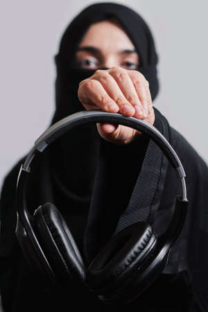 Muslim woman in traditional hijab clothing holding black wireless headphonesの写真素材