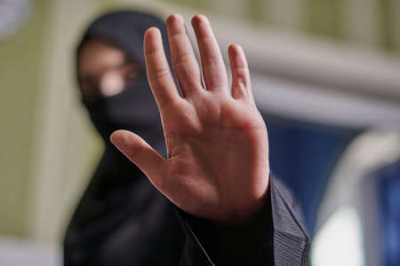A Muslim woman in traditional black clothing nikab showing stop hand gesture. Role of women in Islamic world. Domestic violence, discrimination of Muslim women. Stop domestic violence against womenの写真素材