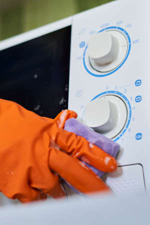 Woman in rubber gloves cleaning microwave oven with sponge in kitchen. Cleaning microwave in the kitchenの写真素材
