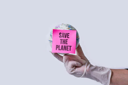 Hand in medical gloves holds a globe with note - save the planet over white backgroundの写真素材