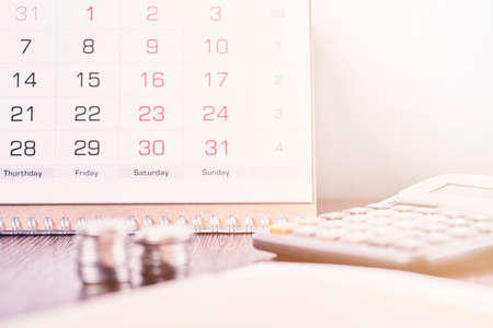 Calendar, calculator and stack of coins in office. Deadline concept. Calendar, coins and calculator on table. Business, finance, taxes, accounting, wages, payroll or money planning conceptsの写真素材