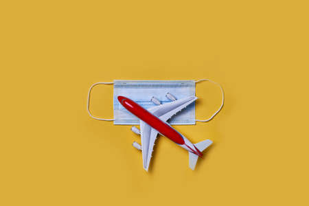 Airplane toy model and face mask on yellow background. New flight rules or travel restrictions. Plane model and face mask. Flight impact of coronavirus or COVID-19 concept. Safe travel during pandemicの写真素材